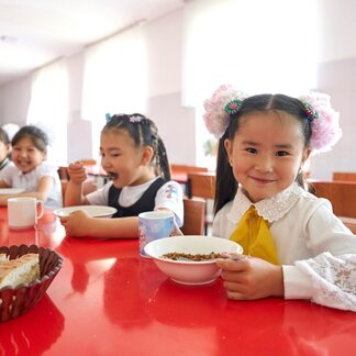 Smiling schoolgirls eat bowls of food. Photo: WFP