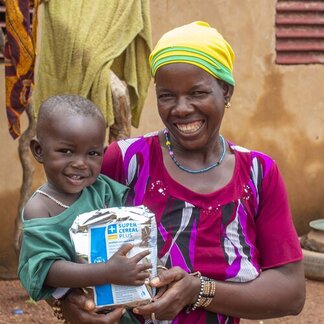 A child in his mom's lap is holding a WFP cereal pack