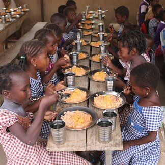 Rows of cHildren on either side of a table eating a meal