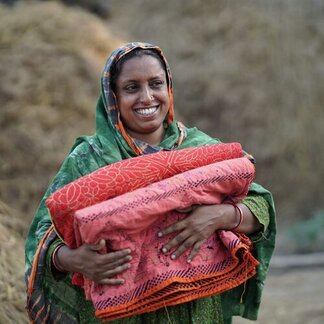 Bangladeshi woman in green headscarf smiles as she carries bundles of red material
