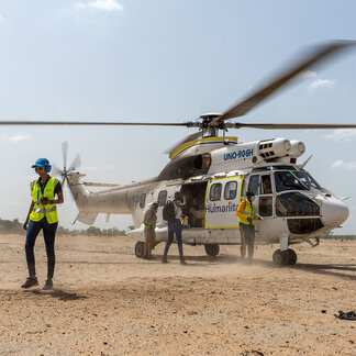 A woman in a vest walking away from WFP helicopter which is about to depart