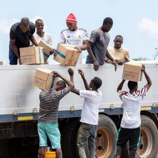 Group unloading cardboard boxes from a truck during a relief operation in a rural setting.