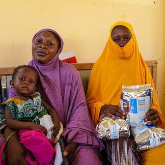 Caregivers and a child receive specialised nutritious food at a health facility, supporting treatment and prevention of malnutrition.