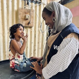 WFP staffer looks at a child sat on a table, both are smiling