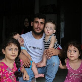 Man in white T-shirt and jeans sits on indoors floor with four children.