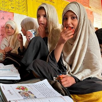 Girls sitting and eating WFP snacks with books in front of them.