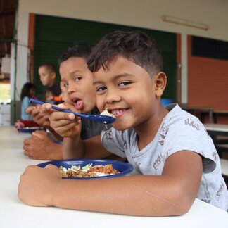 A row of children sitting down and eating a meal.
