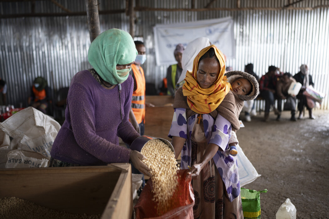 Woman in green headscarf scoops pulses out for a woman in orange headscarf at a WFP food distribution in Ethiopia