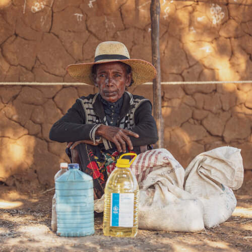 a woman is sitting with the food she received from WFP